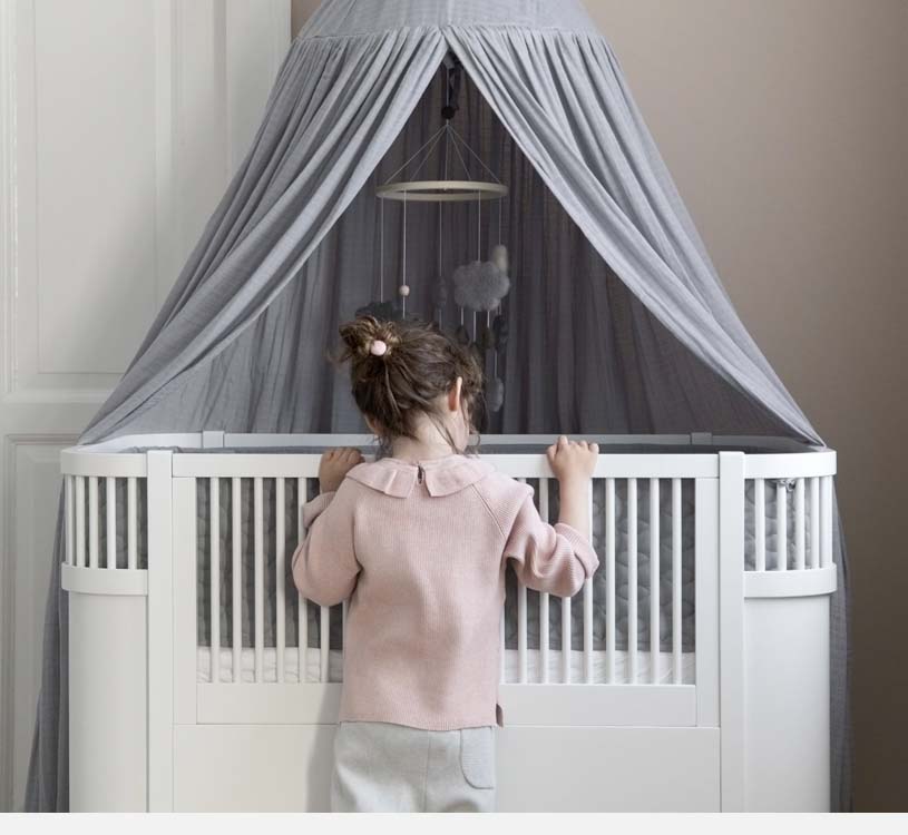 Jente ved hvit sprinkelseng med grå baldakin og uro.