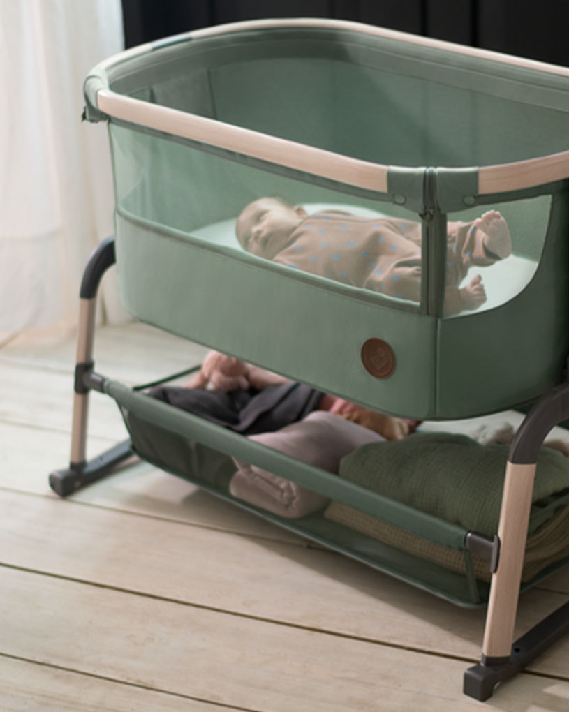 Baby sover i en grønn barneseng med oppbevaringshylle under.