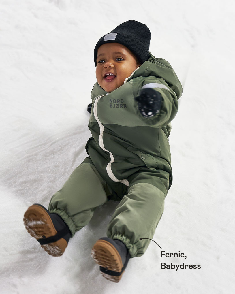 Barn i grønn vinterdress sklir på snøen.