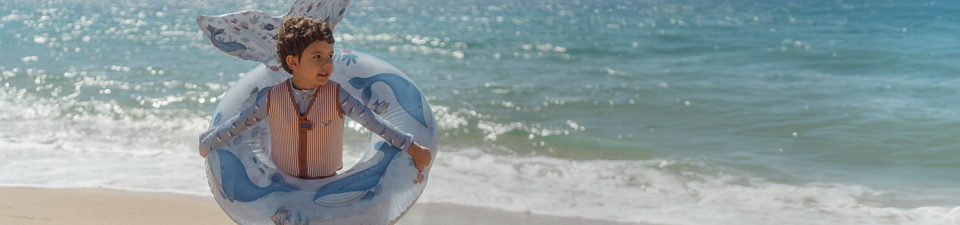 Barn på strand med badering, hav bak. Tekst: "Nytt for sesongen".