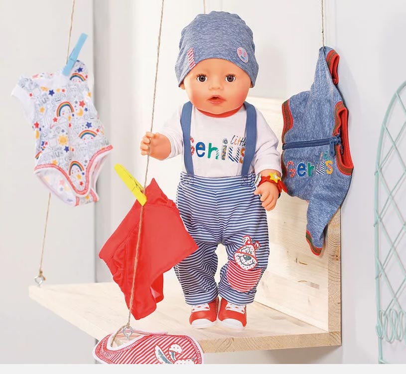 Dukke med stripete bukser og lue på hylle, omgitt av barneklær.