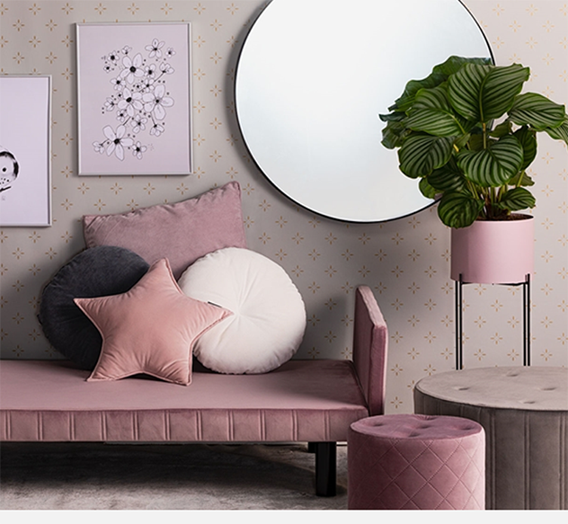 Rosa sofa med puter, rundt speil og plante i potte.