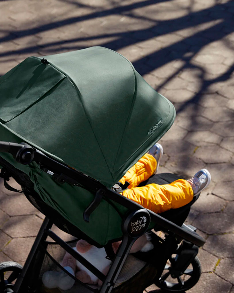 Barnevogn med grønt tak og barn i gule bukser.