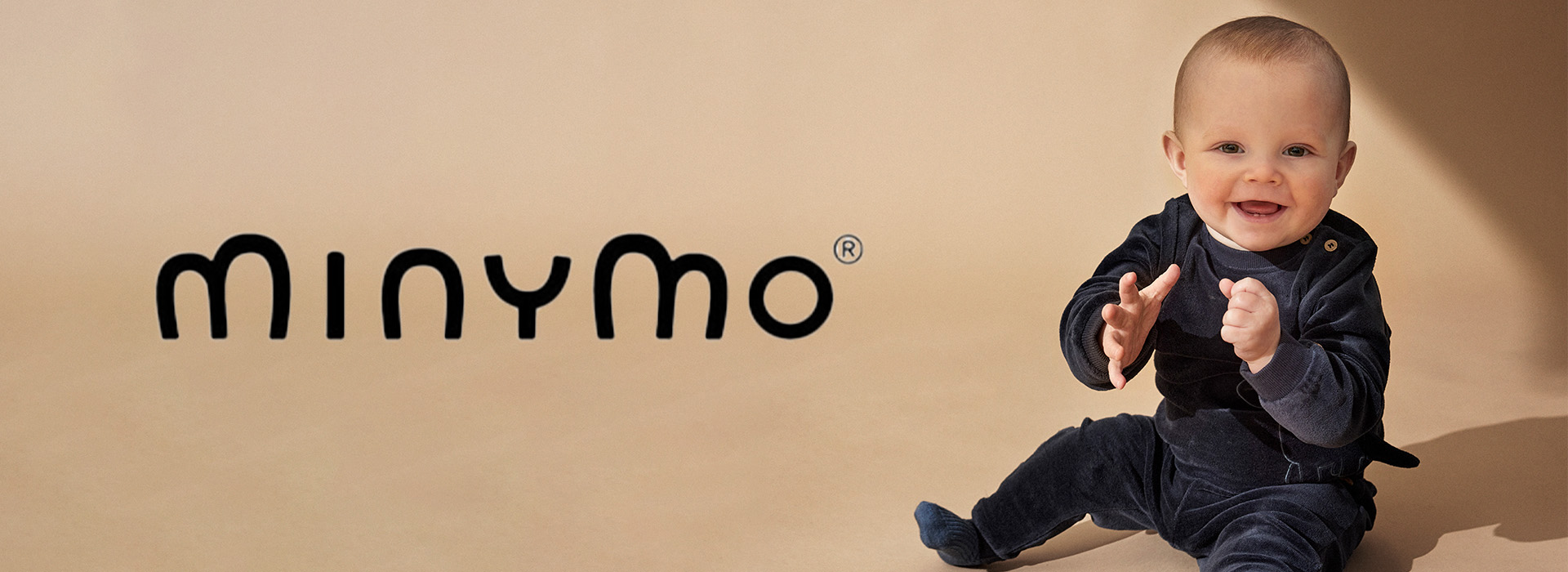 Baby i mørk dress på beige bakgrunn ved siden av Minymo-logoen.