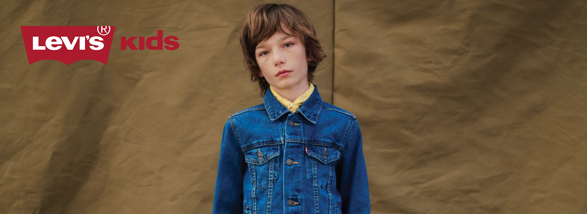 Barn i olajakke foran brun bakgrunn.