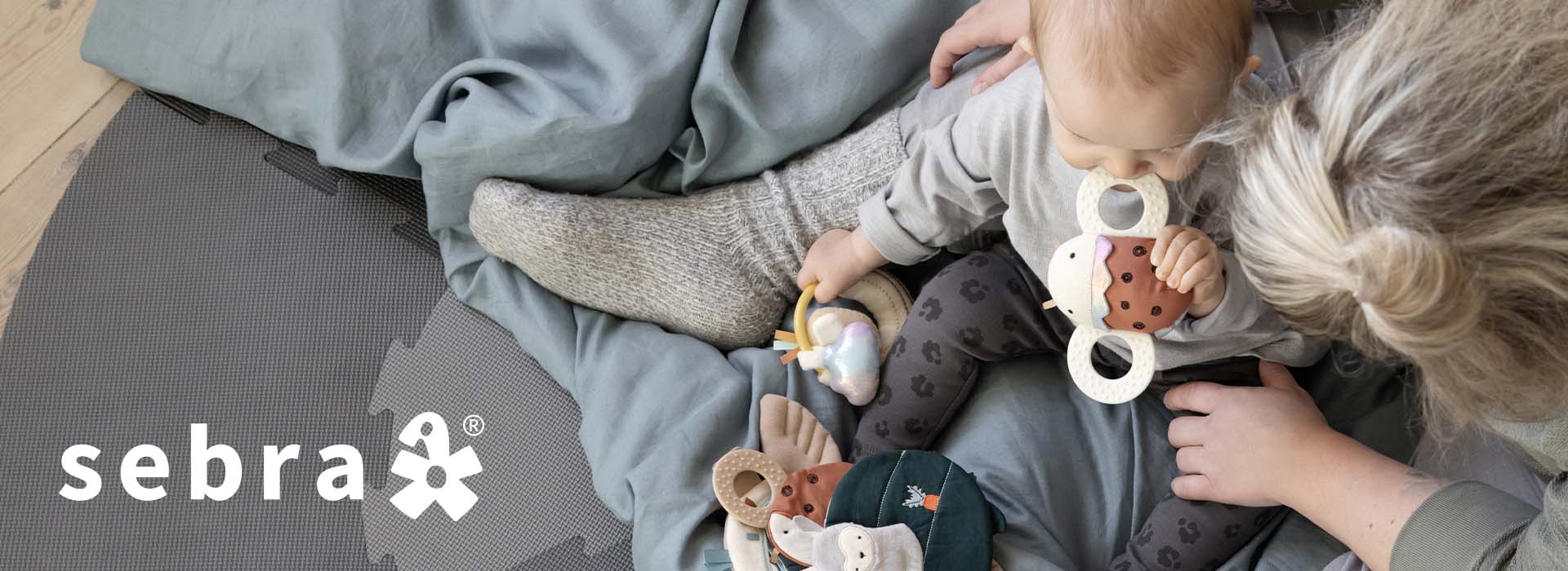 Barn leker med aktivitetsleker på gulvet med en voksen ved siden av.