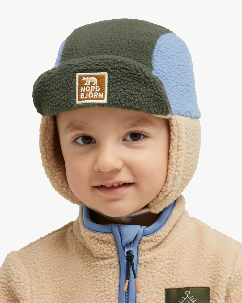 Barn med oransje hatt med teksten 'NORD BJØRN' mot skogsbakgrunn.