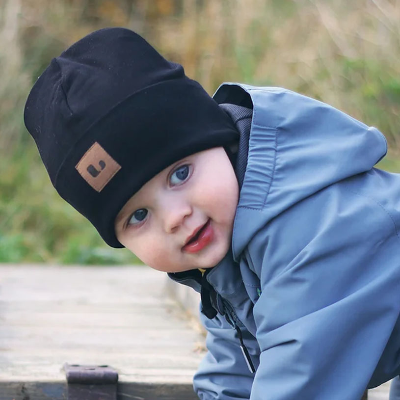 Barn i svart lue og jakke smiler ute.